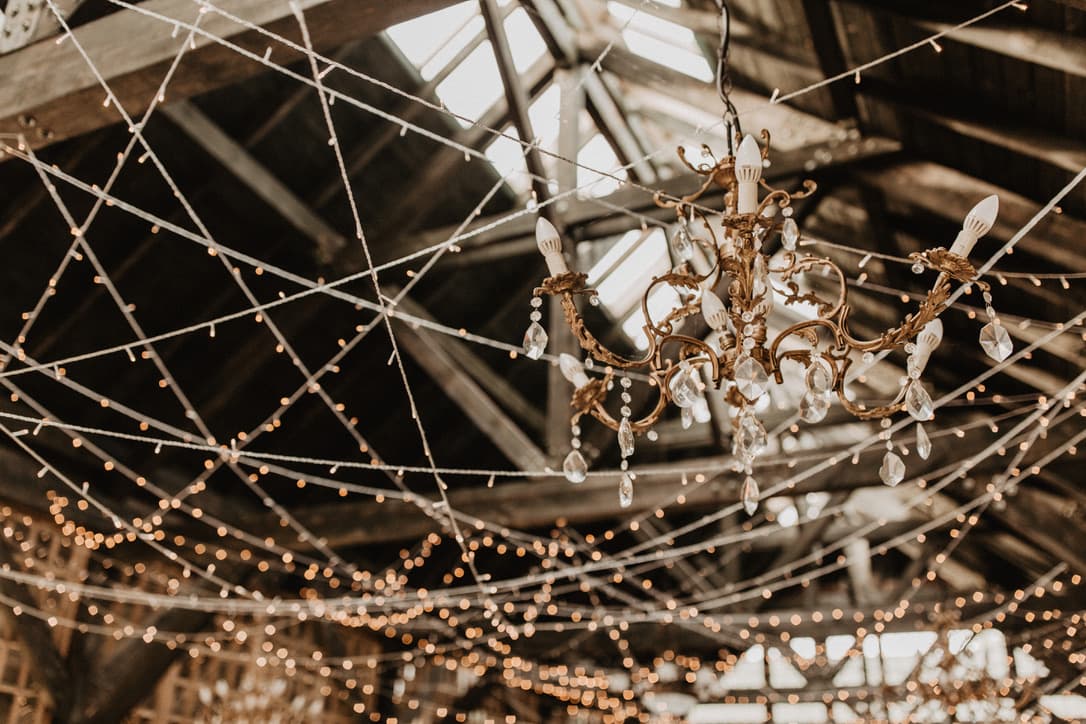 Crystal chandelier suspended under a timber roof strung with fairy lights