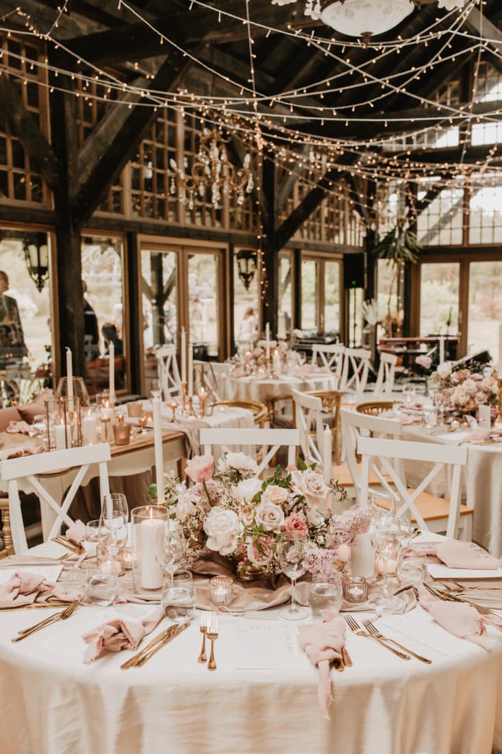 Barn reception with blush round tables beneath a canopy of fairy lights